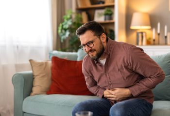 Terrible stomachache. Frustrated handsome young man hugging his belly and keeping eyes closed while lying on the couch at home