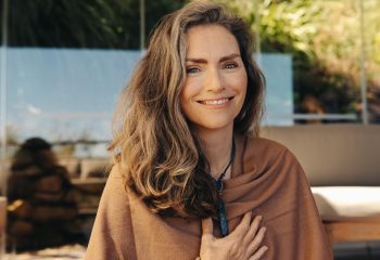 Cheerful senior woman smiling at the camera while wearing a crystal necklace. Happy woman meditating and practicing crystal healing on her chest chakra. Mature woman following a holistic lifestyle.