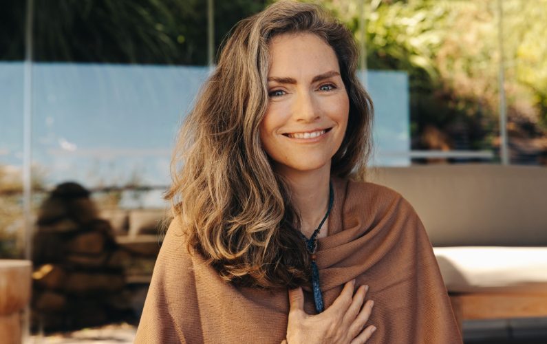 Cheerful senior woman smiling at the camera while wearing a crystal necklace. Happy woman meditating and practicing crystal healing on her chest chakra. Mature woman following a holistic lifestyle.