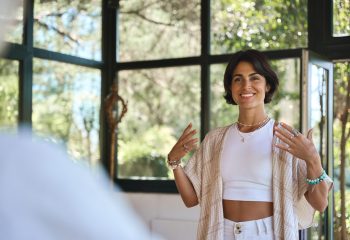 Young happy woman yoga coach training group class yoga meditation session sitting in yoga pose in studio speaking to community teaching people during retreat holistic mind body health therapy.