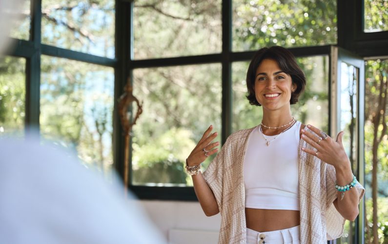 Young happy woman yoga coach training group class yoga meditation session sitting in yoga pose in studio speaking to community teaching people during retreat holistic mind body health therapy.