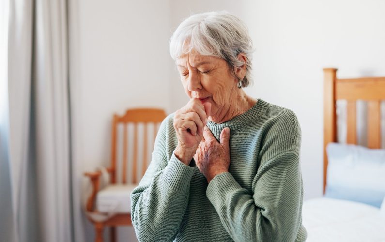 Cough, sick and senior woman on bed in home with allergies, chest infection or sore throat. Illness, retirement and elderly female person with tuberculosis, cold or flu symptoms in bedroom at house