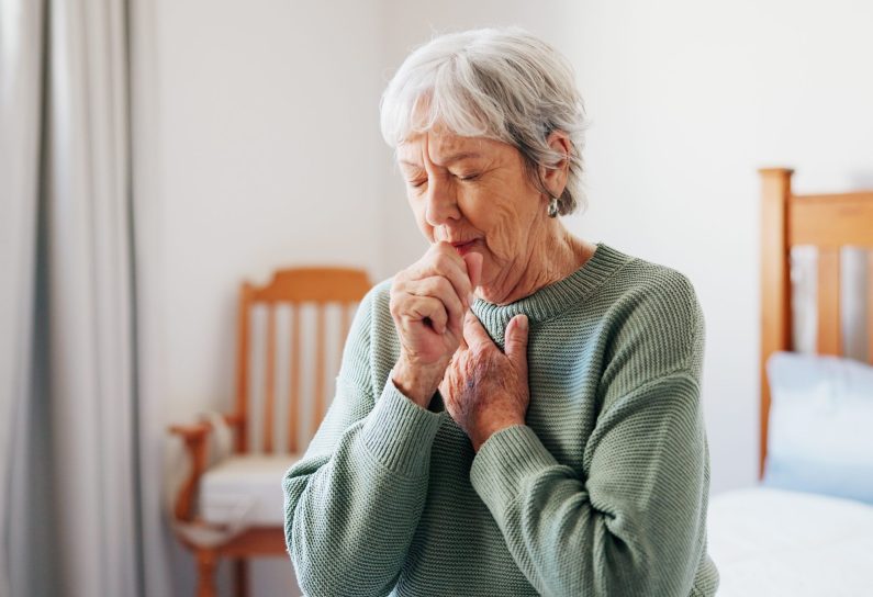 Cough, sick and senior woman on bed in home with allergies, chest infection or sore throat. Illness, retirement and elderly female person with tuberculosis, cold or flu symptoms in bedroom at house