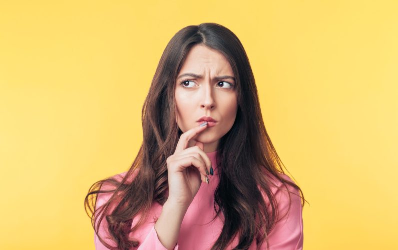 Thoughtful confused woman looking away isolated over yellow background. Doubt concept