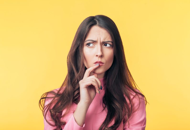 Thoughtful confused woman looking away isolated over yellow background. Doubt concept